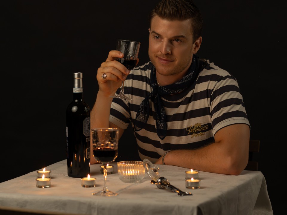Bruno Flütsch sitzt an einem Tisch bei Kerzenlicht mit einem Glas Rotwein in der Hand